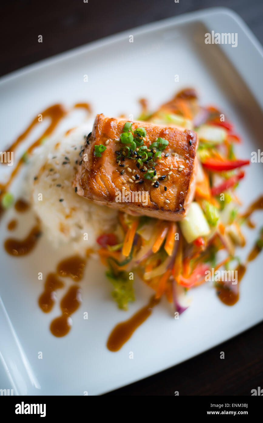 A piece of salmon sitting on top of rice and pickled vegetables on a white plate Stock Photo