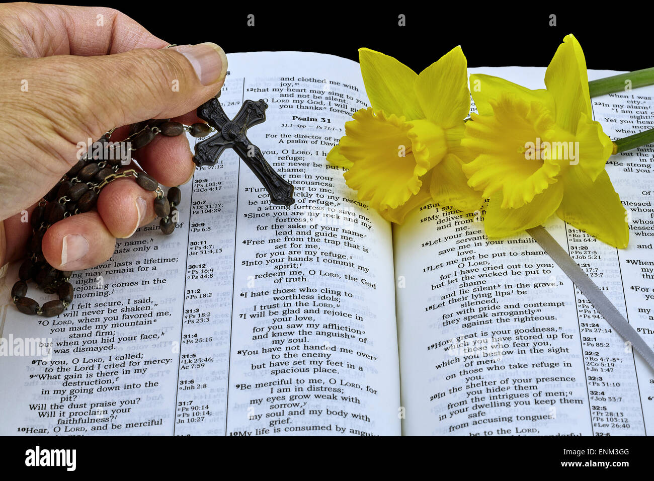 Man holding vintage rosary with crucifix over open Bible with Psalms and yellow easter daffodils symbolizing life Stock Photo