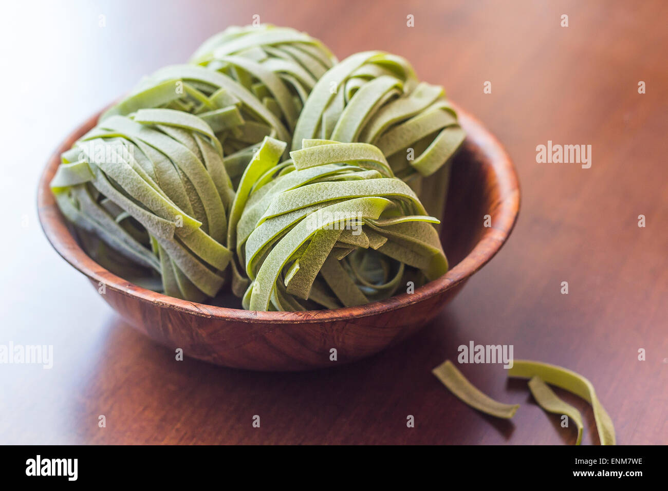 Dry organic spinach fettuccine pasta nests in a wooden bowl Stock Photo
