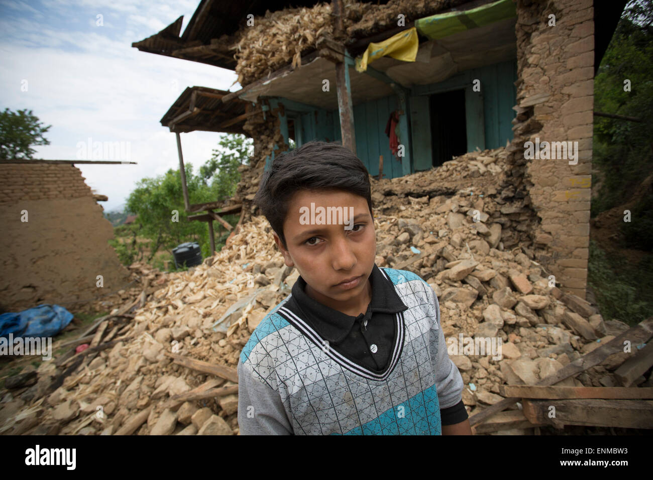 A boy stands in front of his collapsed home in Karvre District, Nepal after the 2015 earthquake. Stock Photo