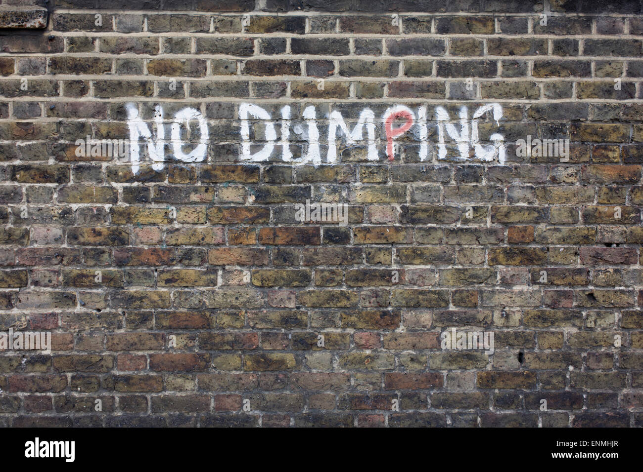 No Dumping writing painted on an urban brick wall in the south London borough of Lewisham, SE5. Stock Photo