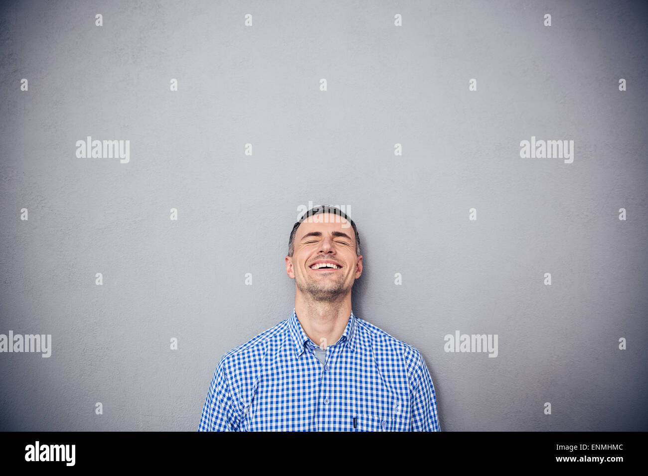 Portrait of a laughing young man over gray background. Leaning on the gray wall Stock Photo