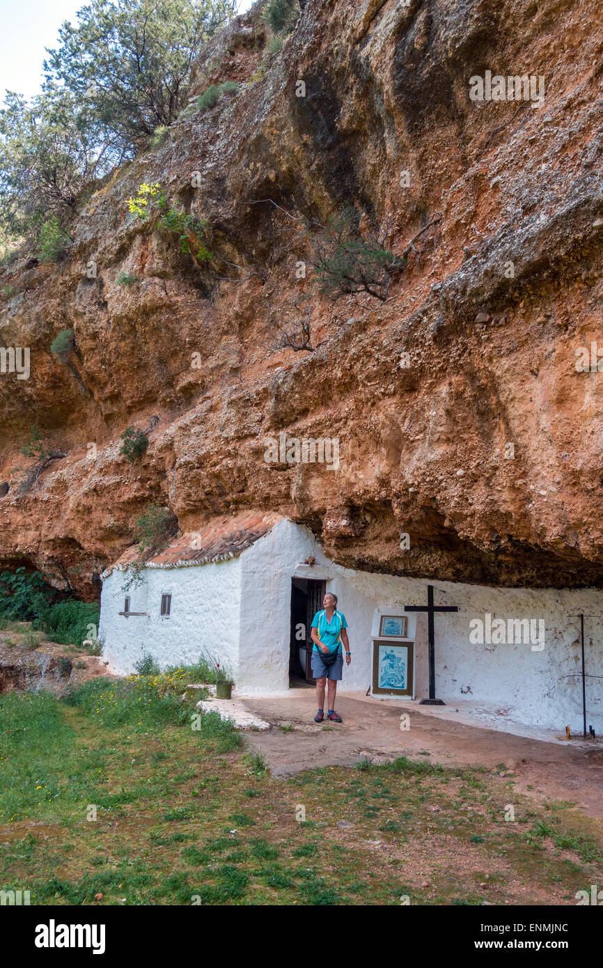 Female figure in shorts by white painted chapel built into cliff face, Greece Stock Photo