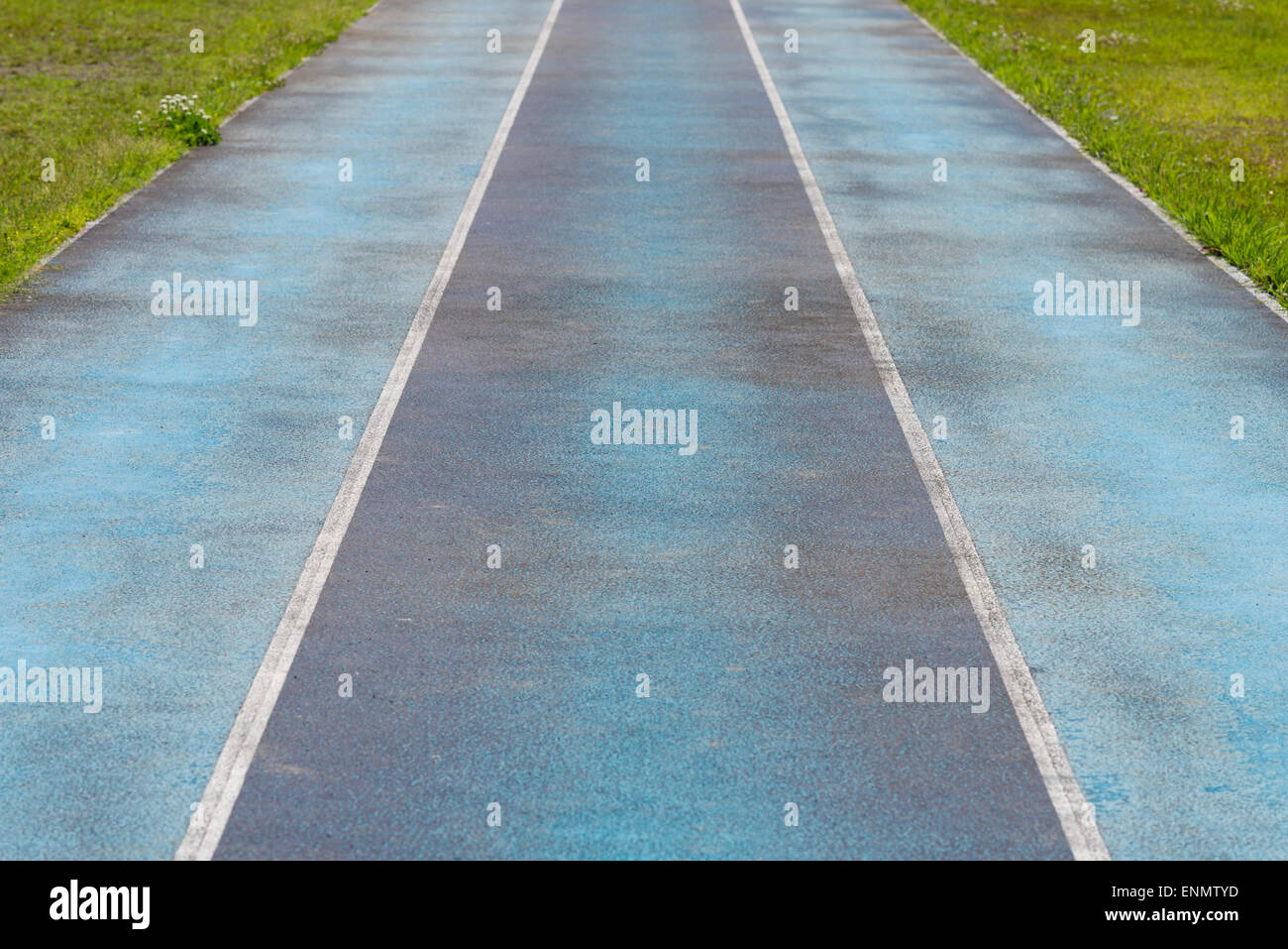 A blue track with three lanes and overgrown grass on either side Stock Photo