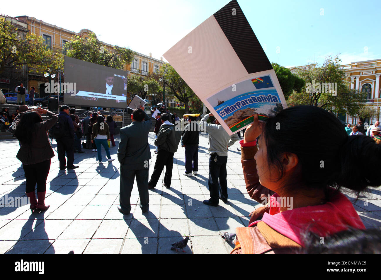 La Paz, Bolivia, 8th May 2015. A local girl shades herself from the sun using a banner with the hashtag #MarParaBolivia (Sea for Bolivia) while watching Bolivia's final presentation to the International Court of Justice in The Hague on a giant projection screen in Plaza Murillo. The initial hearings for Bolivia's case reclaiming access to the Pacific Ocean against Chile have been taking place in the ICJ this week, the hearings were to debate the Chilean objection that the court doesn't have the jurisdiction to judge the case. Credit:  James Brunker / Alamy Live News Stock Photo