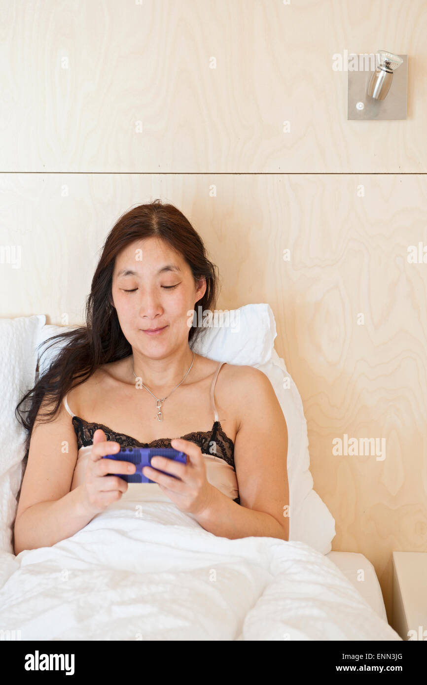 Woman checking her cell phone in bed at summercottage in Laugar in north Iceland Stock Photo