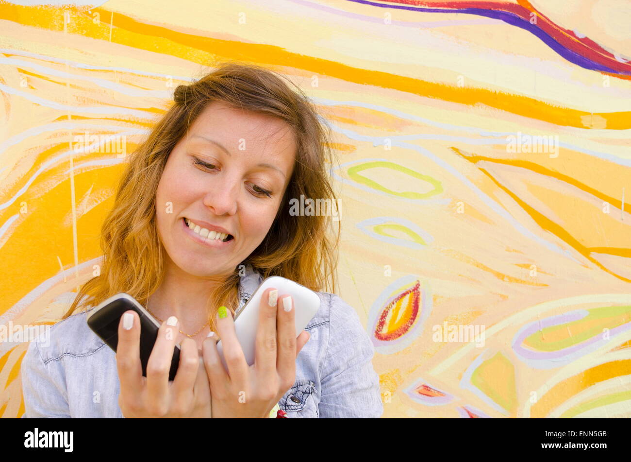 Happy girl looking at two smart phones against a colorful backdrop Stock Photo