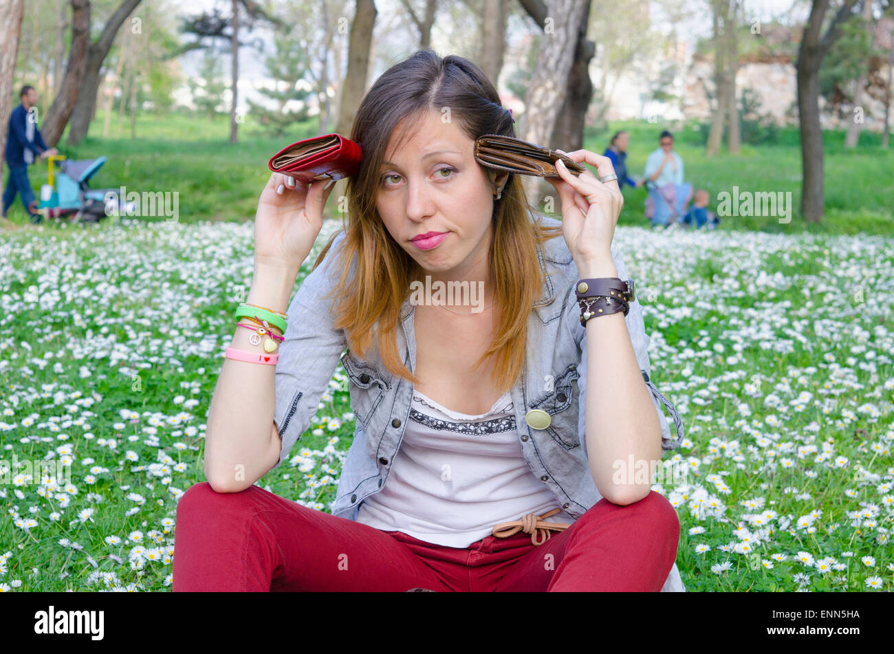 Broke brunete sitting in the park among the daisies with two wallets in her hands Stock Photo