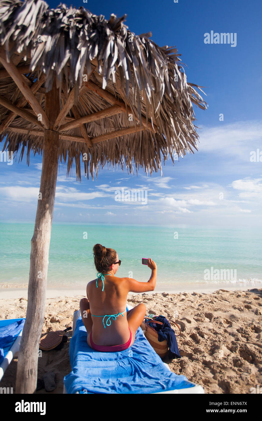 A young woman takes a picture with her smartphone while relaxing on the beach Stock Photo