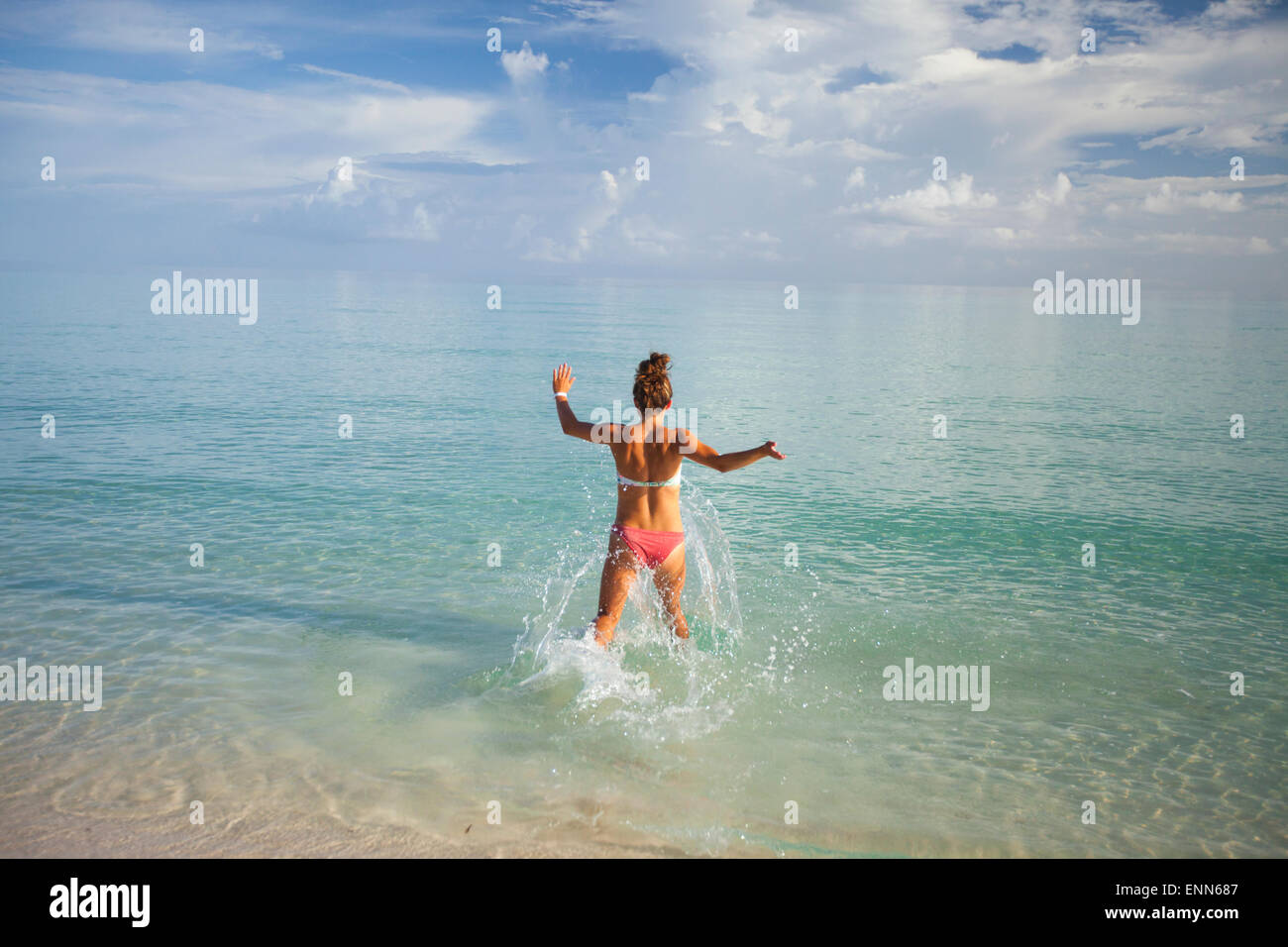 A young woman runs into shallow turquoise water while on vacation in Cuba. Stock Photo