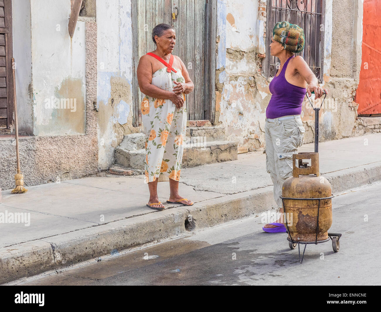 Two Cuban women talking outside, one with hair curlers in her hair and with a two-wheel dolly with a propane tank on it. Stock Photo