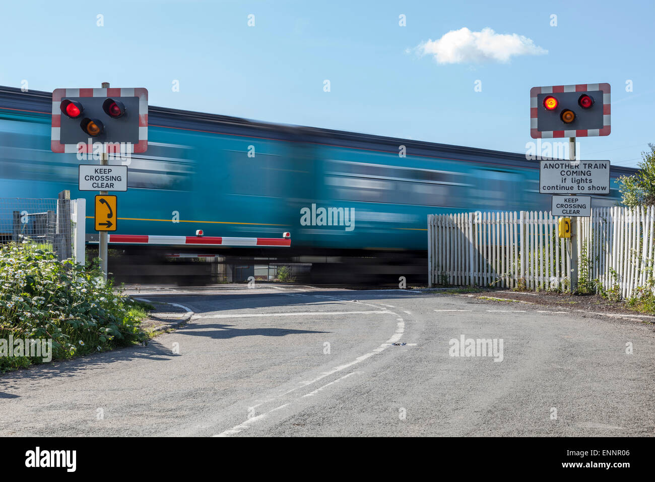 Local train passing through an unmanned half barrier level crossing Stock Photo