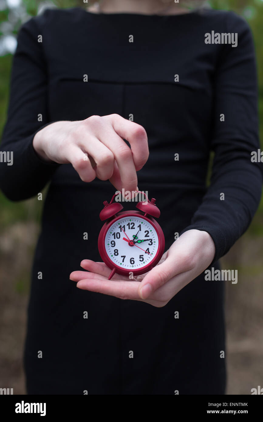 Women in black dress holding red alarm clock by one hand Stock Photo