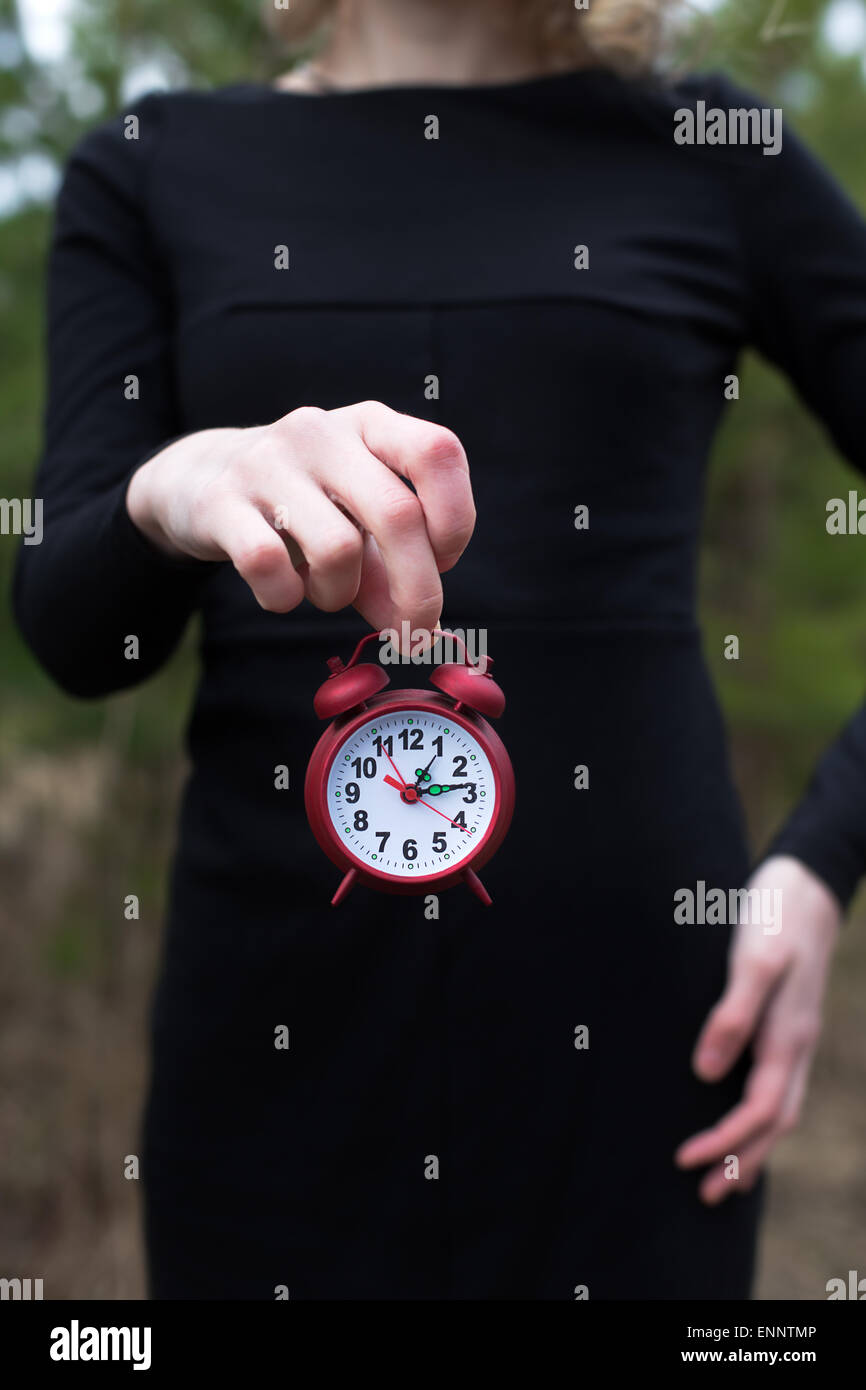 Women in black dress holding red alarm clock by one hand only Stock Photo