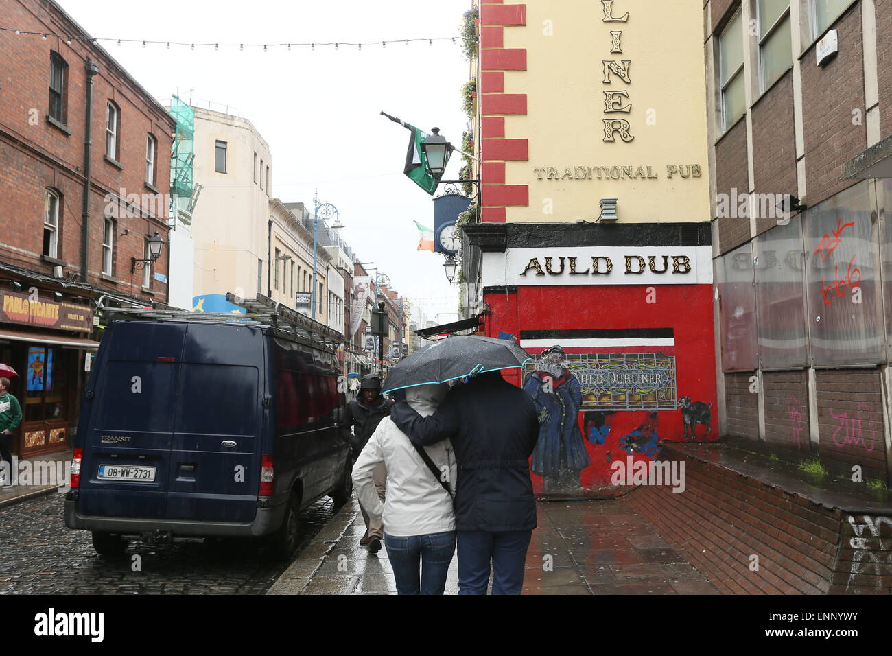 A couple holding an umbrella walk through Temple Bar in Dublin city
