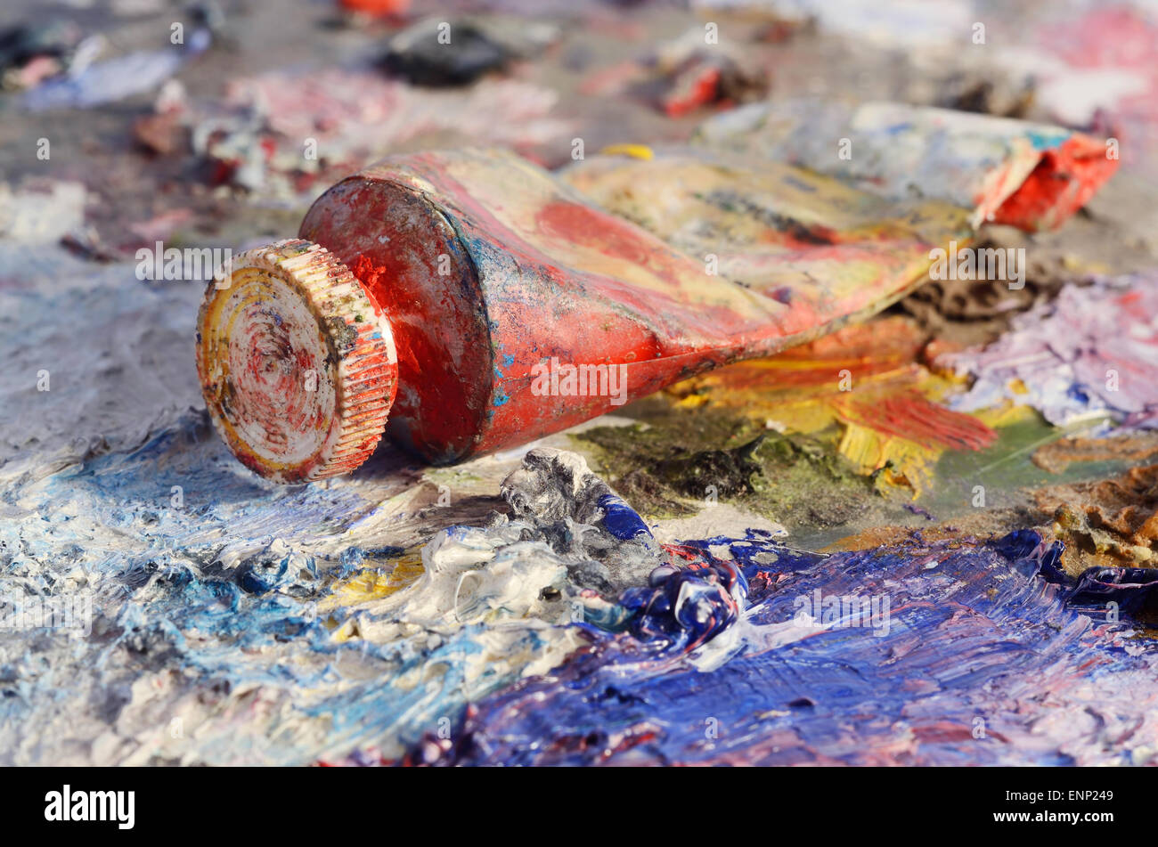 Closeup of old oil paint tube with red colour lying on dirty artistic palette ,background for creative art design Stock Photo