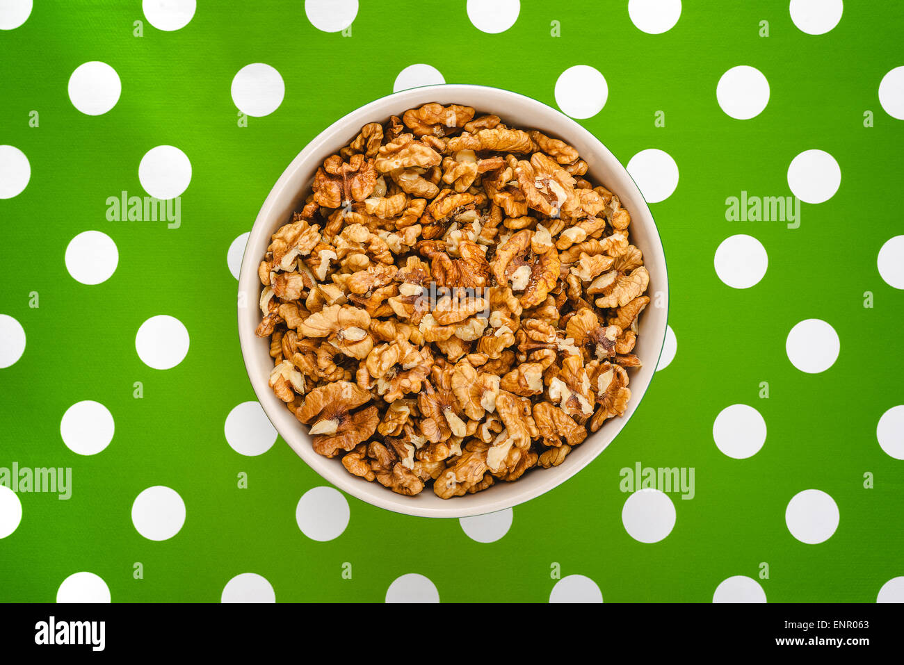 Peeled Walnut Kernels in Ceramic Bowl on Green Polka Dotted Background, Top View Stock Photo