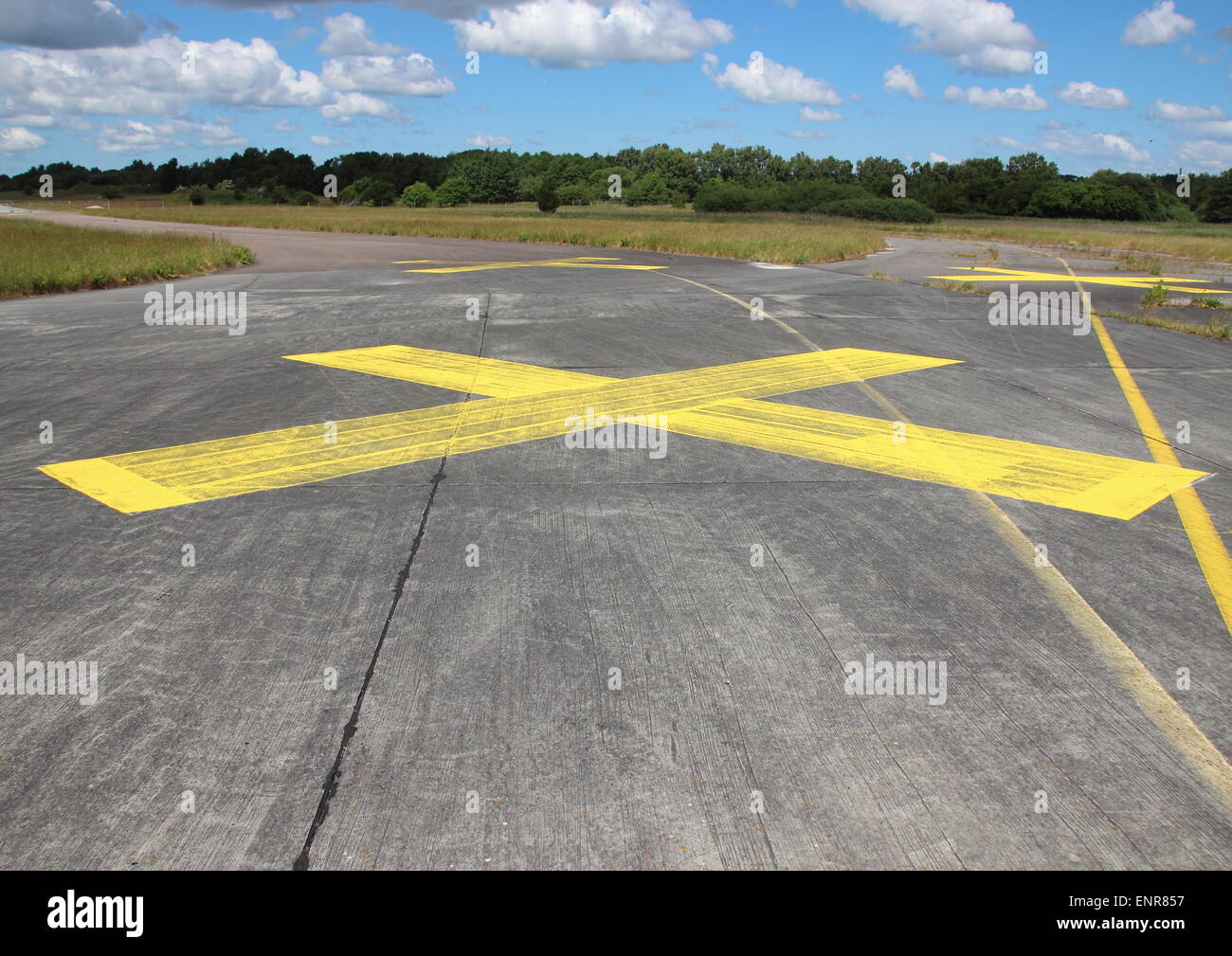 Yellow painted cross on asphalt with clouds in background Stock Photo