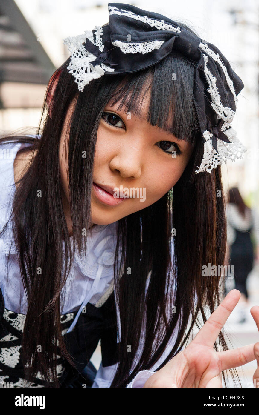 Japan, Kyoto. Costume play girl, Goth Lolita Victorian Maid black outfit. leaning down and smiling, giving peace sign. Close up, face, eye-contact. Stock Photo
