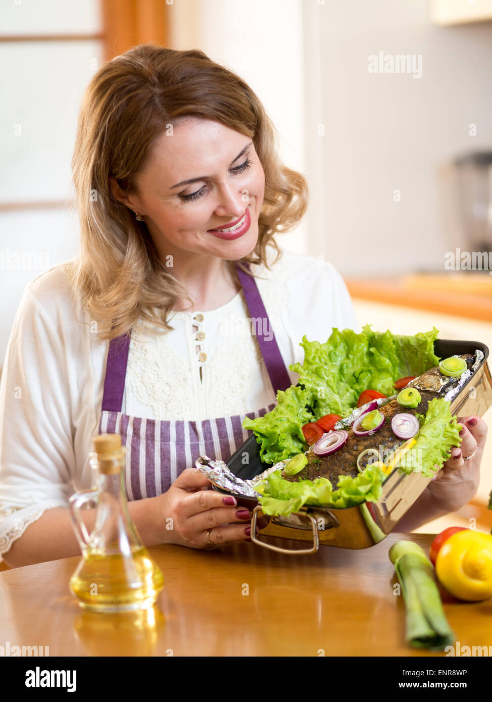 Cook - middle-aged cute woman grill fish in kitchen Stock Photo