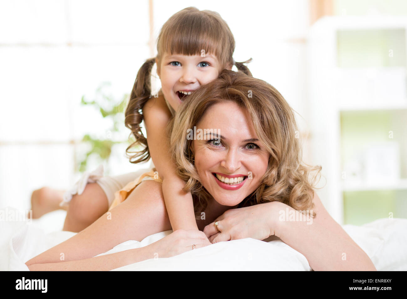 Happy middle-aged mom playing with her kid daughter in bed enjoying