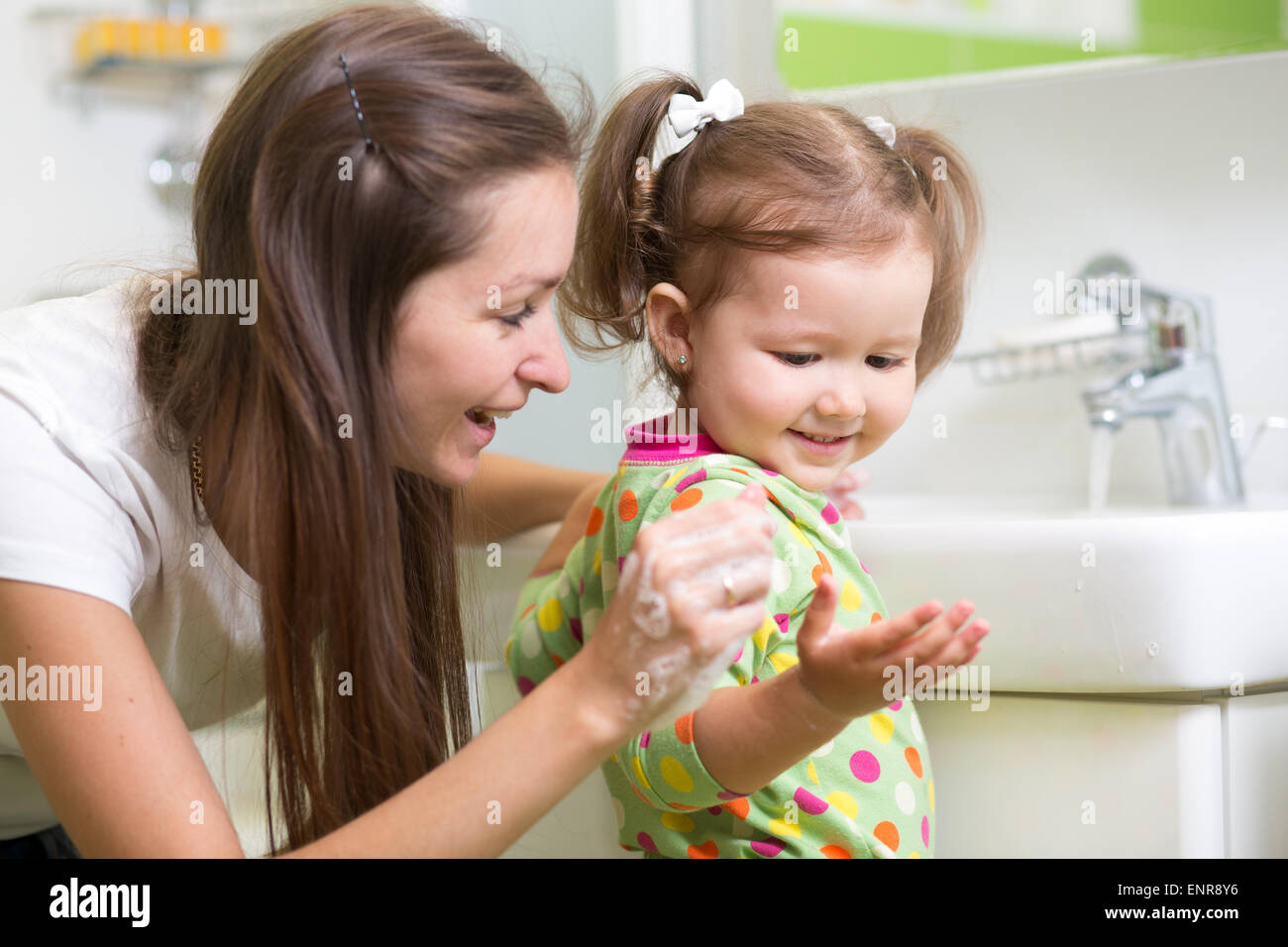 Smiling girl child and her mother washing hands and face with soap in the bathroom. Hygiene