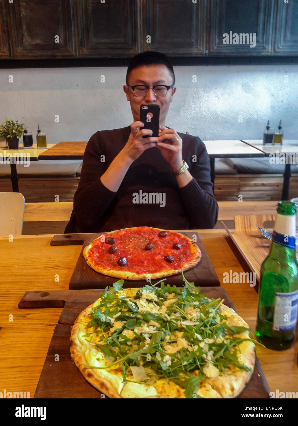 Paris, France. Chinese Tourist Taking Photos with Iphone of Pizza on Table in Italian Restaurant in Bibliotheque District, Pizzeria Stock Photo