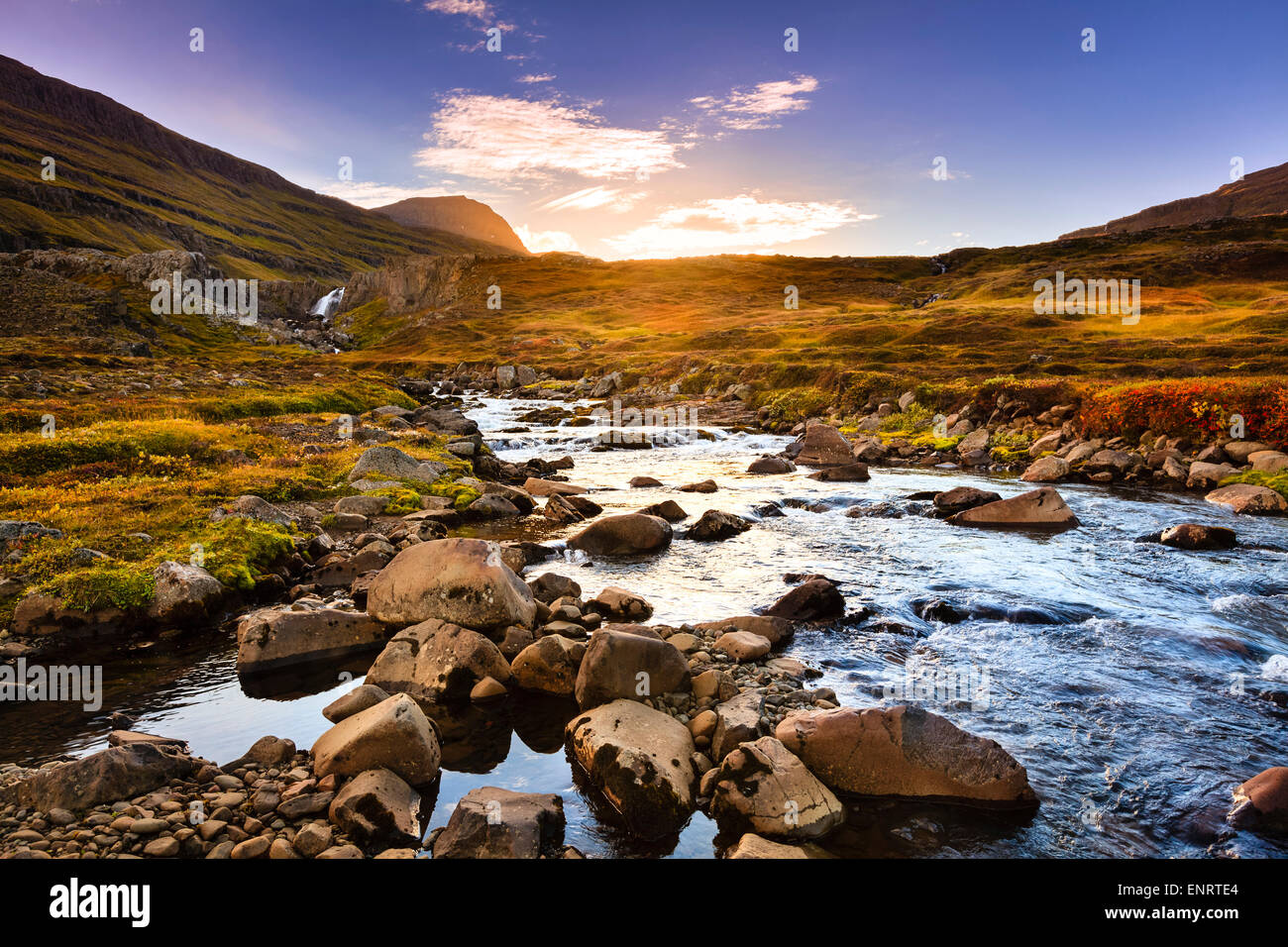 Scenic stream and waterfall in the valley by Seydisfjordur fjord at sunset Stock Photo