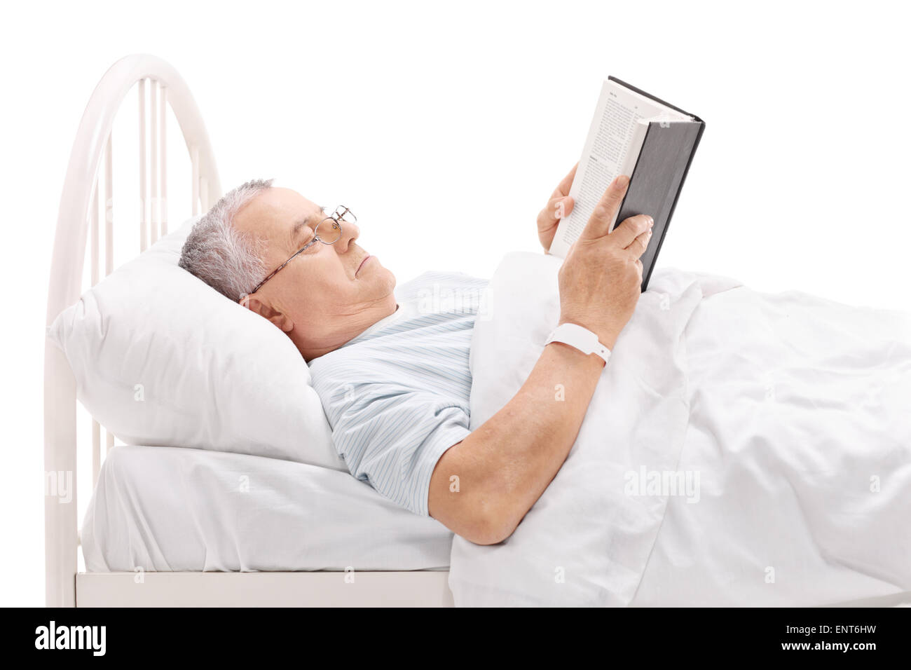 Mature patient reading a book and lying in a hospital bed covered with a white blanket isolated on white background Stock Photo