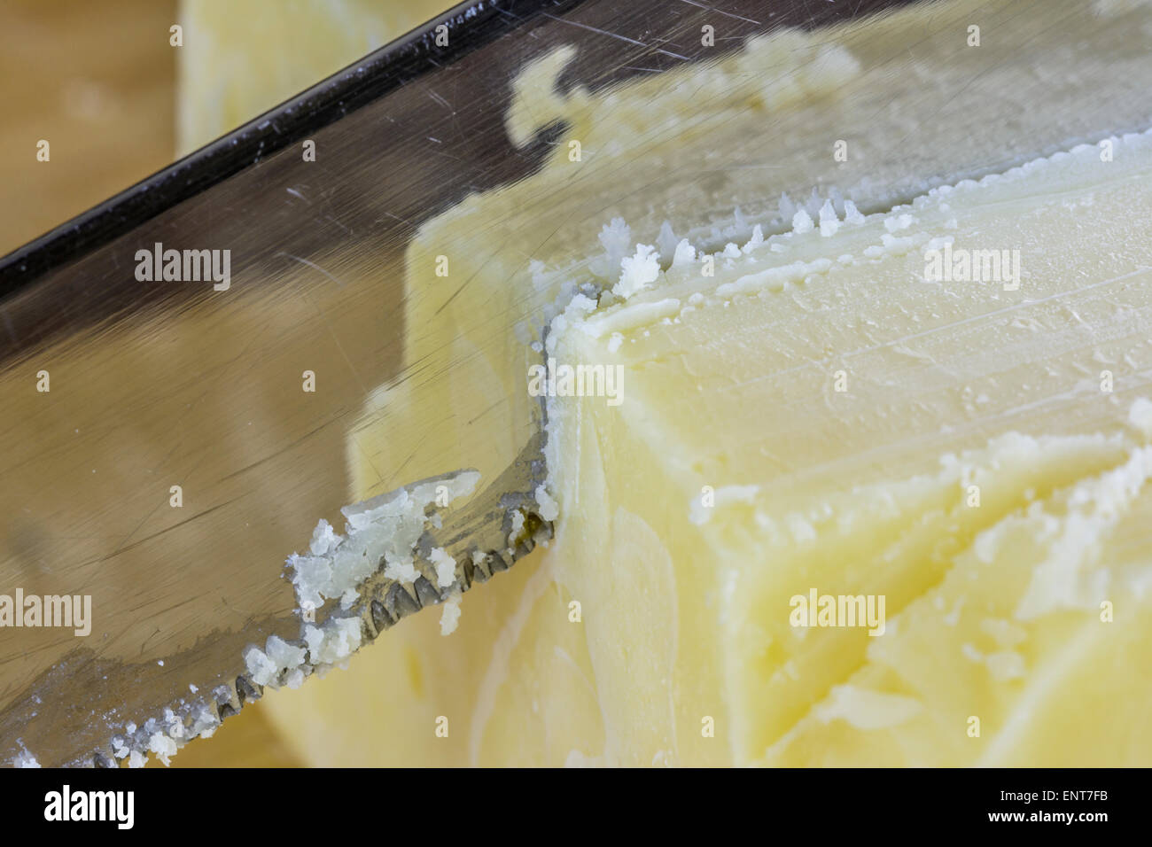 Knife cutting through yellow cheddar cheese with a reflection in the knife. Stock Photo