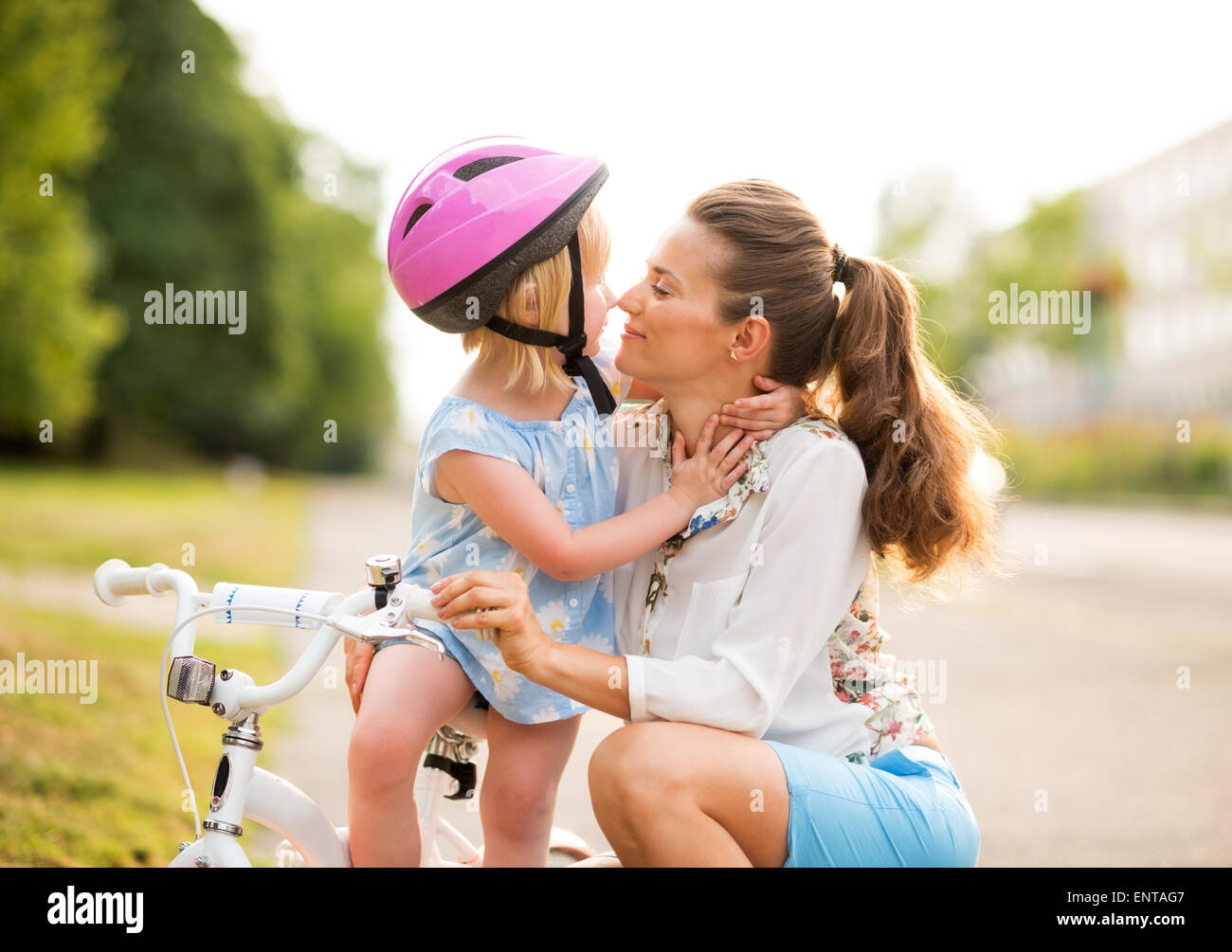 Eskimo kisses between a proud mother and daughter, who has just learned how to ride her bicycle. The mother kneels lovingly next Stock Photo