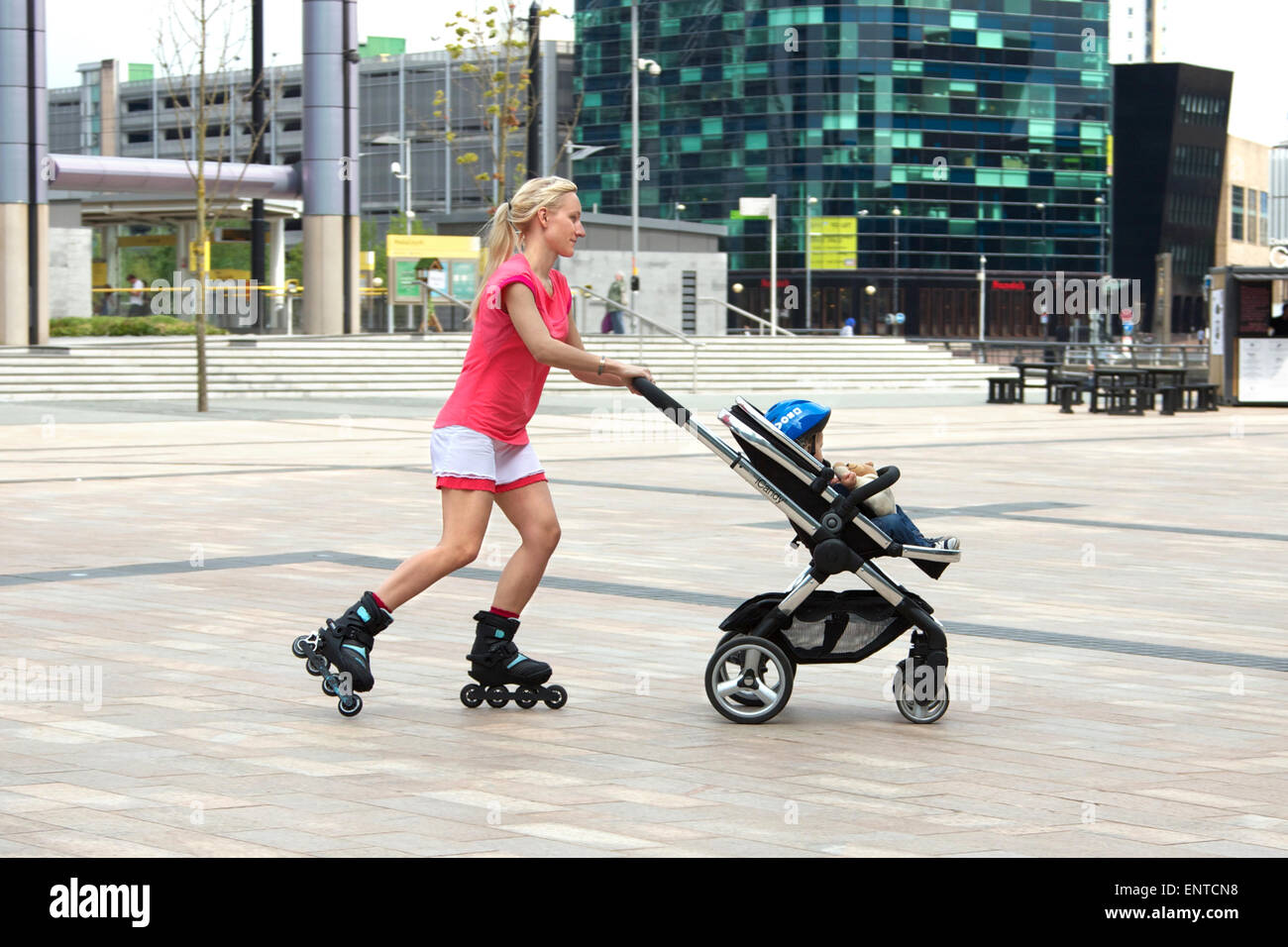 Young woman roller-skating with her child in a push-chair, Media City, Salford, England Stock Photo