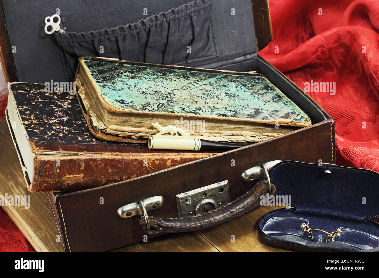 Old books, ivory cigarette holder, key and pince-nez in a retro suitcase Stock Photo