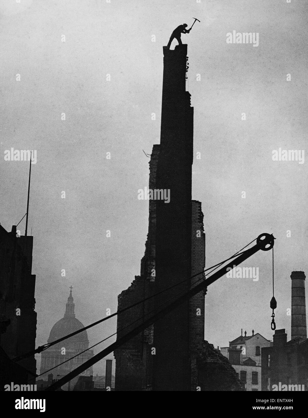 Workman James Woods demolishing a chimney stack with his pickaxe in the shadow of St Paul's cathedral, after the building was damaged in an air raid during the Second World War. March 1942. Stock Photo
