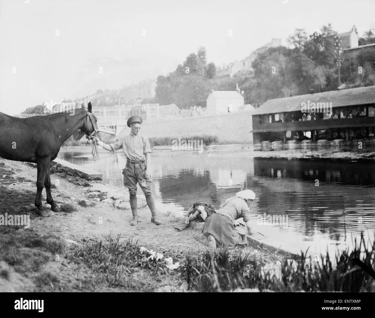 A British soldier seen here with his horse on the banks of an un-named French river watches on as a French women completes the soldiers laundry. Circa 1915 Stock Photo