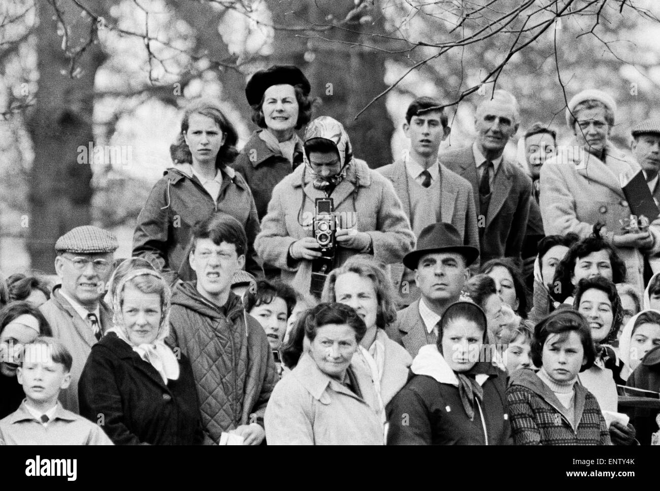 Queen Elizabeth II taking pictures on her Roliflex camera at Badminton Horse Trials with her children Princess Anne and prince Charles watching in the crowd. 12th April 1965. Stock Photo