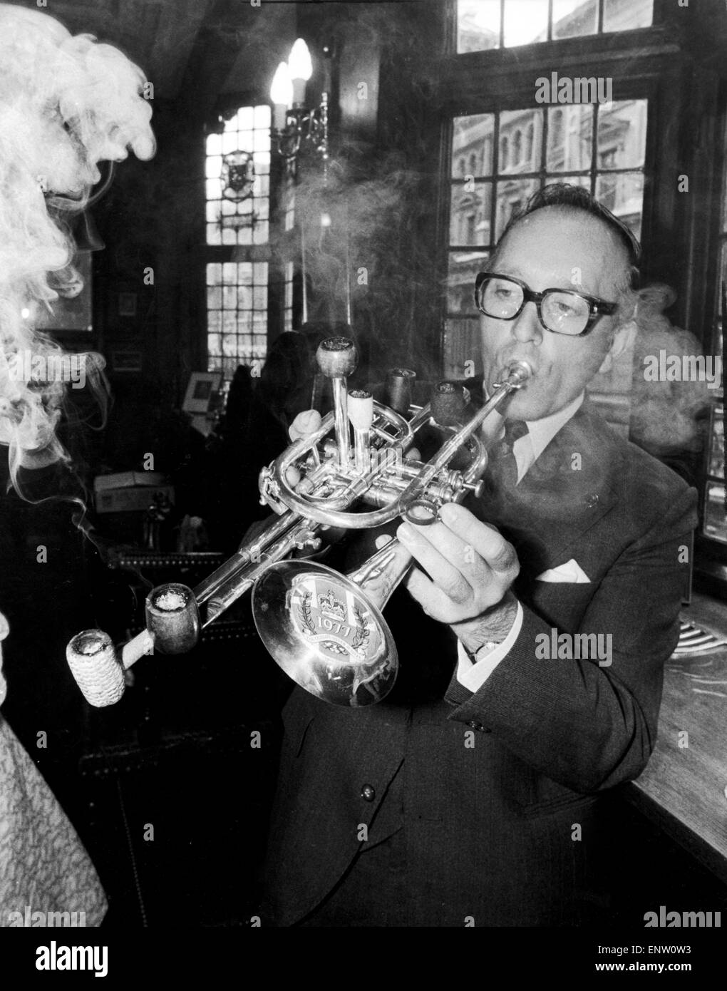 Mr Brian Cole winner of the Remarkable Pipe Contest seen here smoking / playing his Silver Jubilee Fanfare Pipe, a trumpet with six pipes attached at the Prince Henry's in Fleet Street. 26th July 1977 Stock Photo