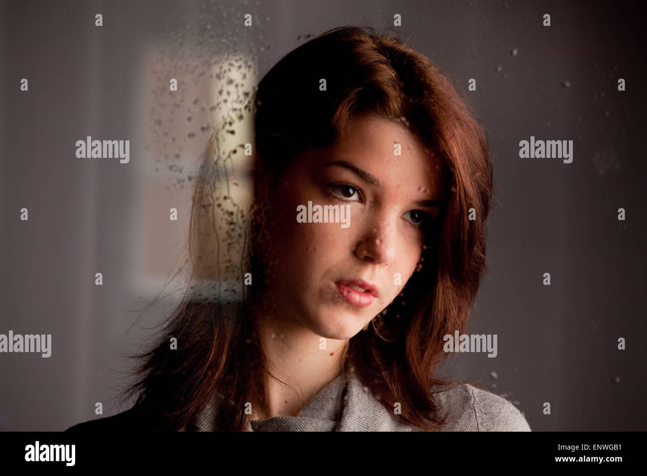 Young woman looking sadly through window glass Stock Photo