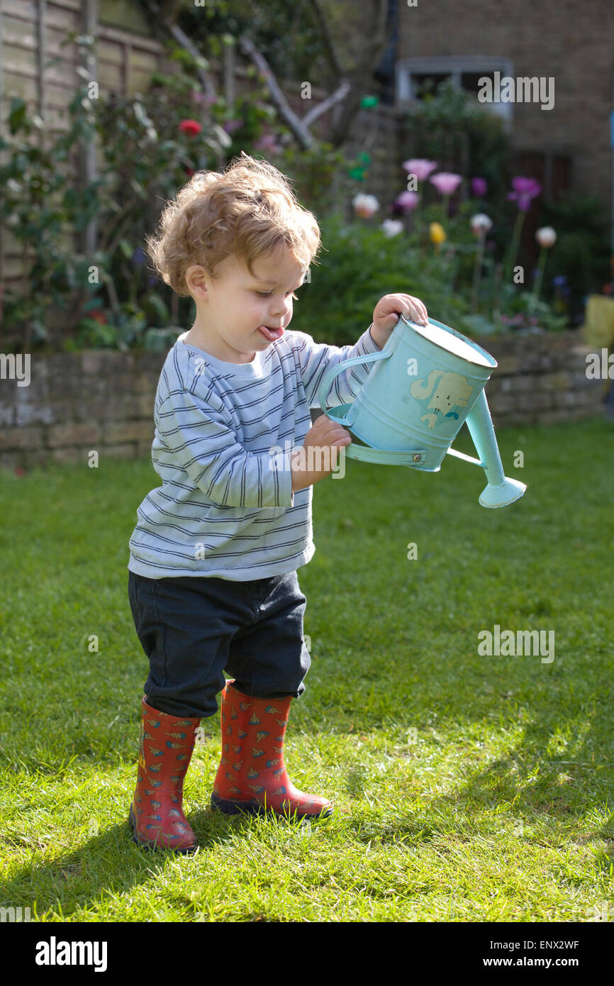 Cute adorable caucasian toddler boy playing holding broom at backyard in  garden outdoors. Child little helper in t-short and shorts having fun  sweeping and cleaning yard near house at countryside Stock Photo