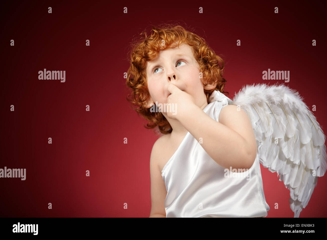 Portrait of the little boy with wings behind the back on a red background Stock Photo