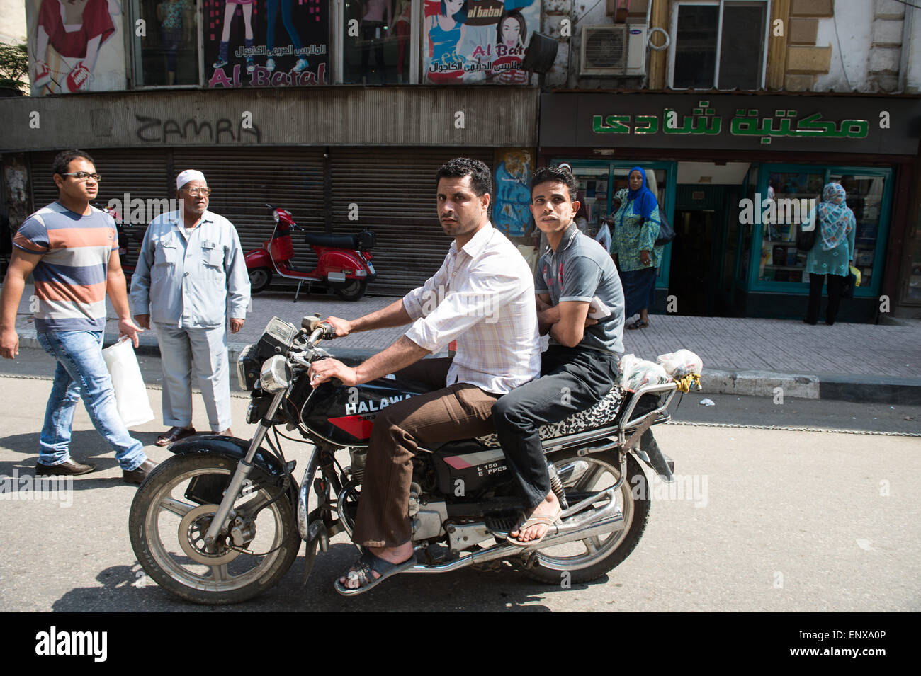 Two men ride on a motorcycle without protective clothing or helmets in