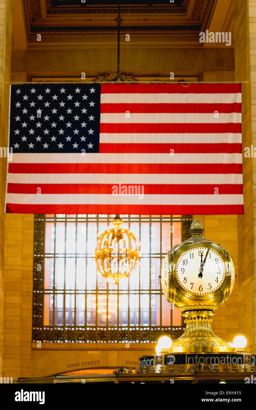 USA, New, York, Manhattan, The Central Information four sided clock in Grand Central Terminal main concourse with the Stars and Stripes flag hanging down from the ceiling behind. Stock Photo