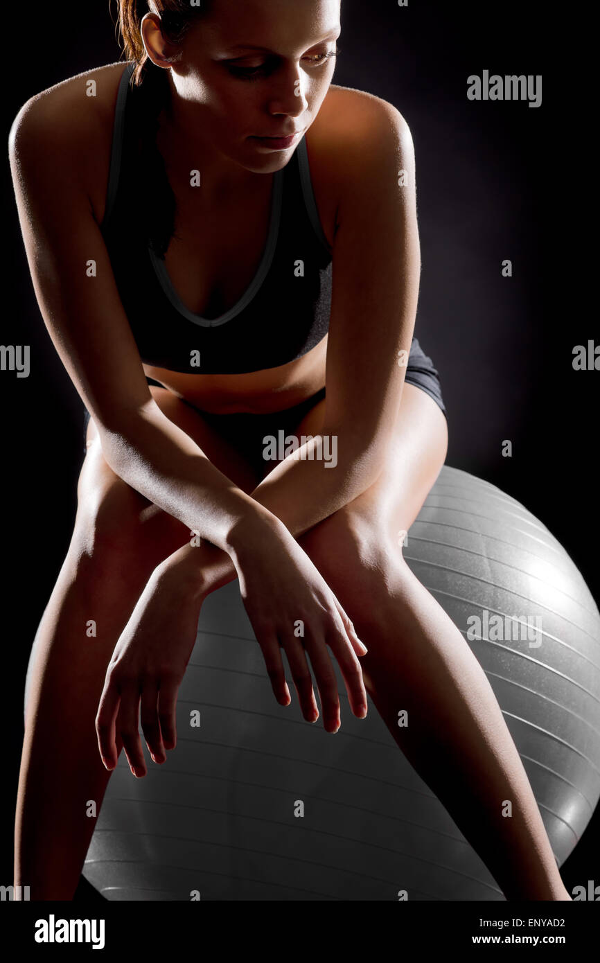 Thoughtful young woman relaxing on fitness ball Stock Photo