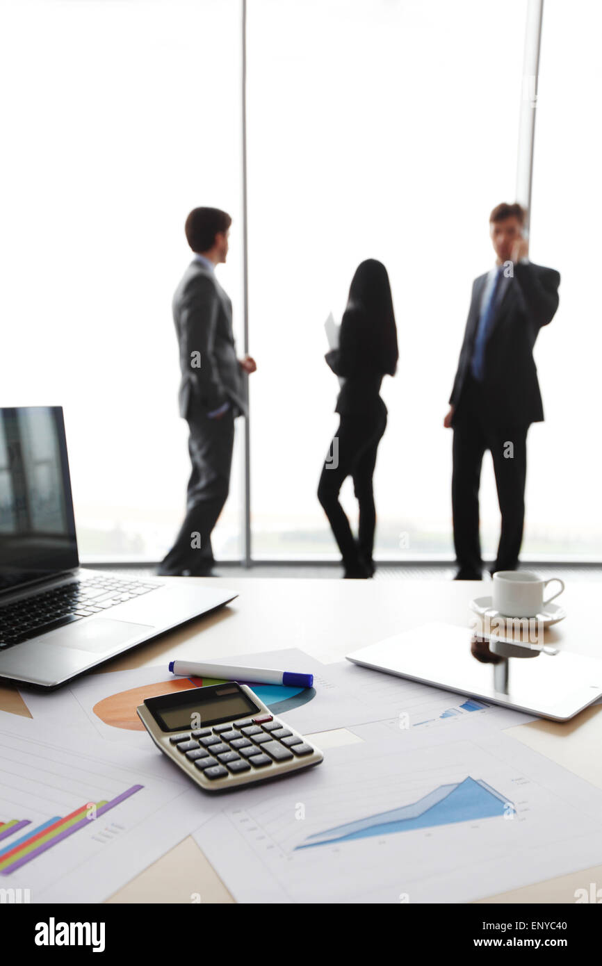 desk with laptop and finance report with business people in background Stock Photo