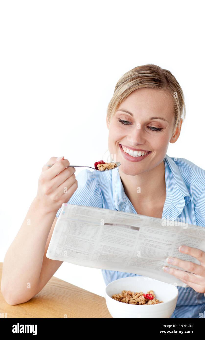 Glowing woman eating cereals while reading newspaper against white ...