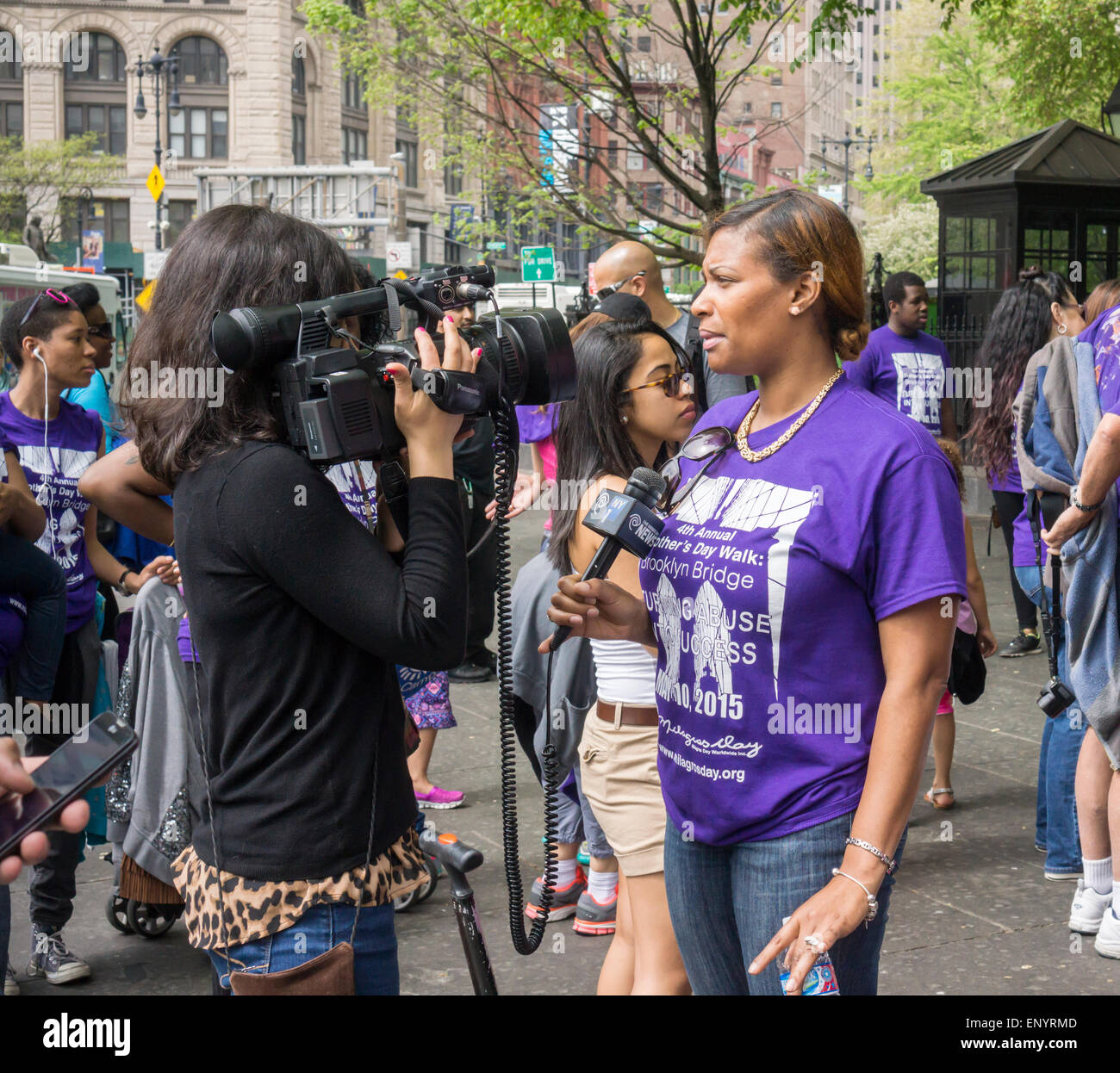 A participant in the  Milagros Day Worldwide Mother's Day Walk against domestic violence is interviewed by Time Warner Cable NY1 in New York on Mother's Day, Sunday, May 10, 2015. Several hundred men, women and children, some of them victims,  participated in their warm up pep rally and walked across the bridge to raise money and awareness for the victims of domestic violence. (© Richard B. Levine) Stock Photo