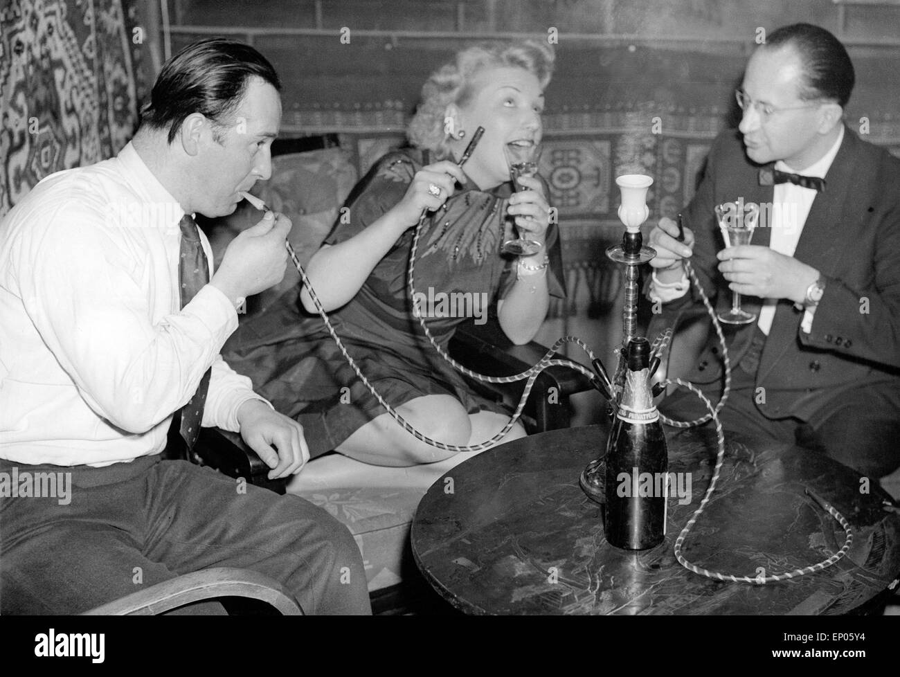 Gäste in einem Nachtclub auf der Reeperbahn in Hamburg genießen ein Glas Sekt zu ihrer Wasserpfeife, 1950er Jahre. Guests of a n Stock Photo