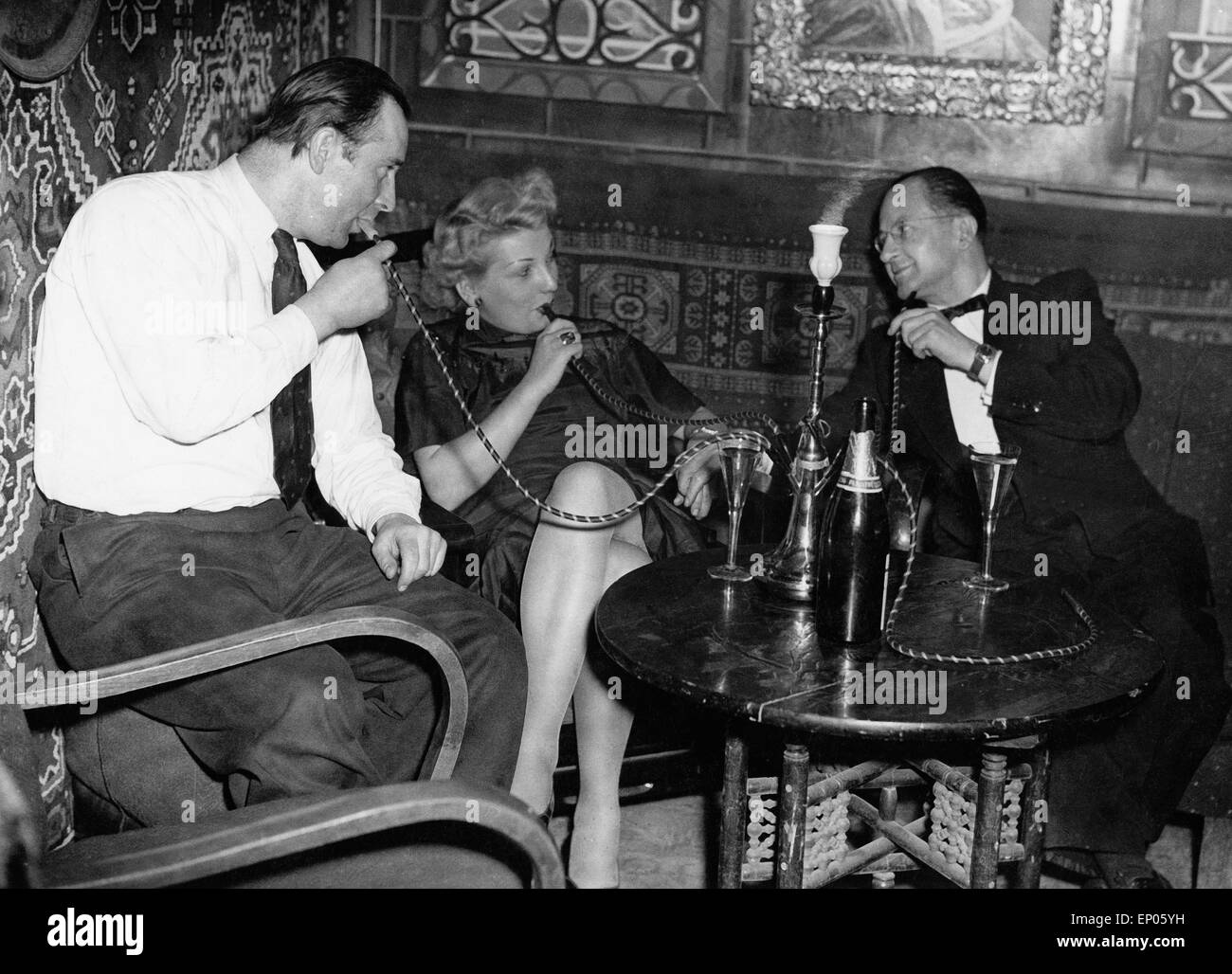 Gäste in einem Nachtclub auf der Reeperbahn in Hamburg genießen ein Glas Sekt zu ihrer Wasserpfeife, 1950er Jahre. Guests of a n Stock Photo