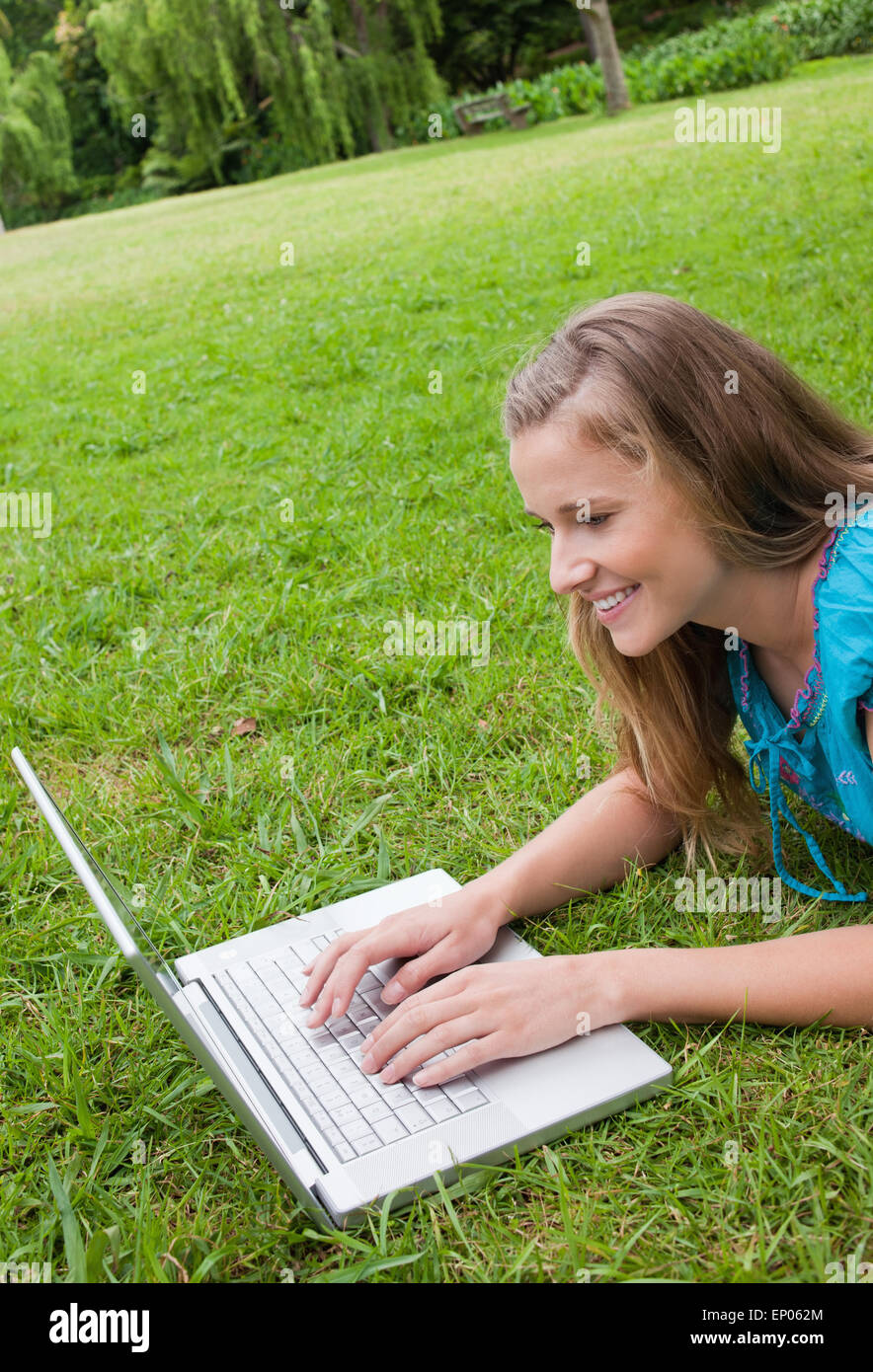 Smiling young woman lying in a park while working on her laptop Stock ...