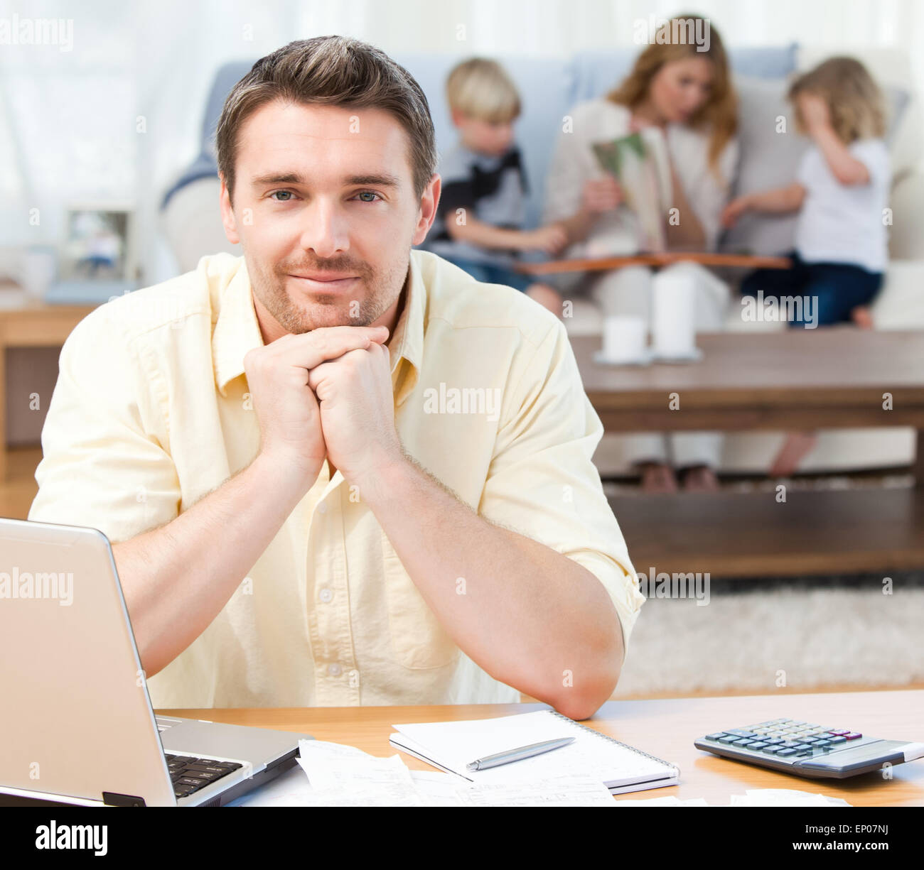 Man calculating his bills while his family are on the sofa Stock Photo